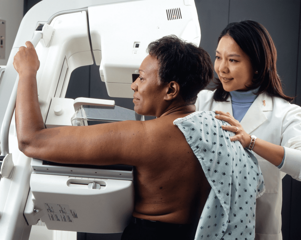 Black woman sits at mammogram machine with female doctor.